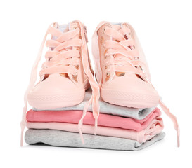 Stylish child shoes and stack of clothes on white background