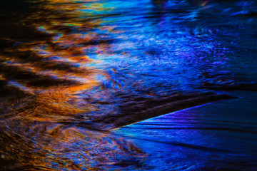 Warm and cool colors mixing and reflecting on the surface of water with small waves and ripples.