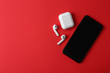 Wireless earphones, mobile phone and charging case on red background, flat lay. Space for text