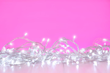 White Christmas lights on wooden table against pink background