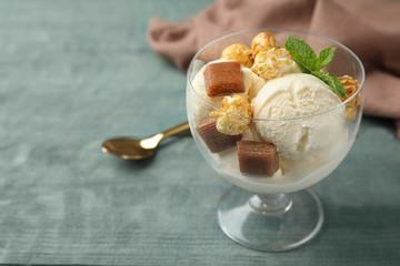 Delicious ice cream with caramel candies and popcorn in dessert bowl on blue wooden table. Space for text