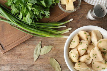 Delicious cooked dumplings with herbs on wooden table, flat lay