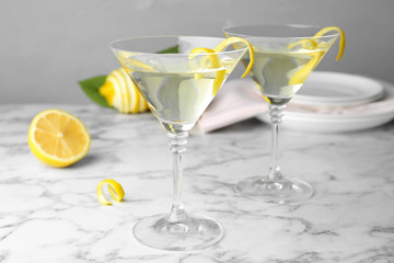 Glasses of lemon drop martini cocktail with zest on marble table against grey background