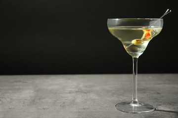 Glass of Classic Dry Martini with olives on grey table against black background. Space for text