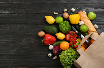 Flat lay composition with overturned paper bag and groceries on black wooden background. Space for...