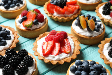 Many different berry tarts on blue wooden table. Delicious pastries - obrazy, fototapety, plakaty
