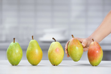 Woman taking fresh ripe pear from table in kitchen, closeup
