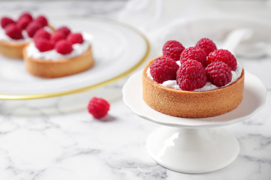 Cake stand with raspberry tart on marble table, space for text. Delicious pastries