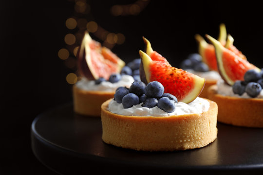 Tarts with blueberries and figs on black table against dark background, closeup. Delicious pastries