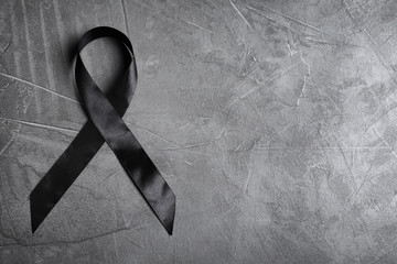 Black ribbon with space for text on grey stone background, top view. Funeral symbol