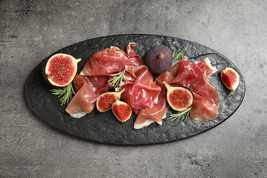 Delicious ripe figs and prosciutto served on grey table, top view