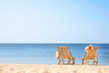 Fototapeta na wymiar Wooden deck chairs on sandy beach near sea