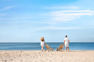 Fototapeta na wymiar Young couple near deck chairs on sandy beach