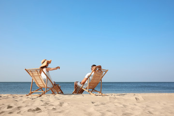 Fototapeta na wymiar Young couple relaxing in deck chairs on beach