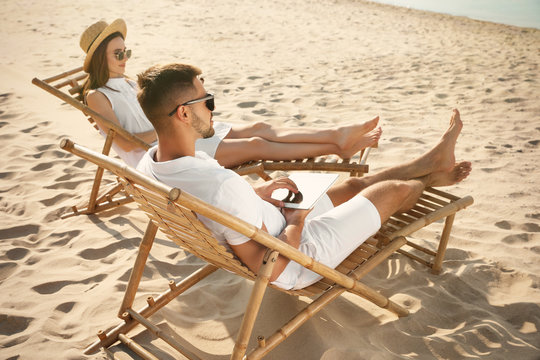 Young couple relaxing in deck chairs on sandy beach - Powered by Adobe
