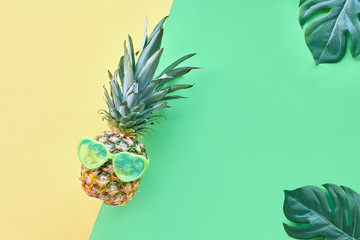 Funny pineapple in heart-shaped sunglasses on geometrc paper with exotic leaves