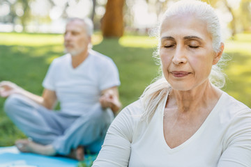 Yoga at park. Close up shot of senior couple sitting in lotus pose on green grass in calm and meditation