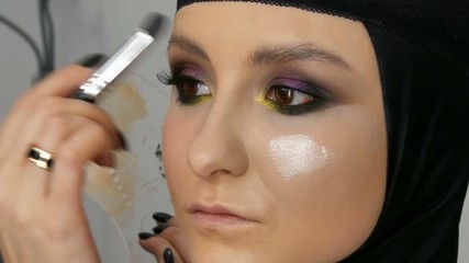 A professional artist makes make-up to a beautiful girl model, feathering powder, highlighter, foundation cream with a special brush for makeup