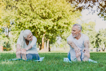 Fototapeta premium Front shot of senior couple stretching in park and exercising outdoors