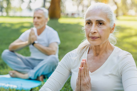 Yoga at park. Close up shot of senior couple sitting in lotus pose on green grass in calm and meditation