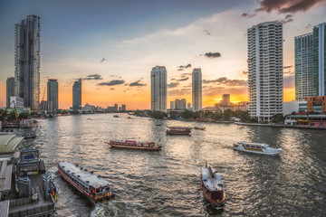 Fototapeta na wymiar Busy Chao Phraya River with Passenger Boats and Skyscrapers at Sunset as Seen from Taksin Bridge in Bangkok, Thailand