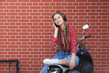 Fototapeta na wymiar Happy young hipster woman listen to music sitting on moped