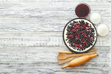 Berry pie with cherry, currant, blackberry, blueberry with kitchenware and ingredients on white wooden table. Cheesecake, top view with copy space.