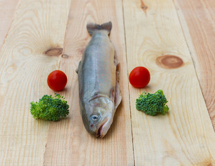 Raw rainbow trout river fish on a wooden background with vegetables