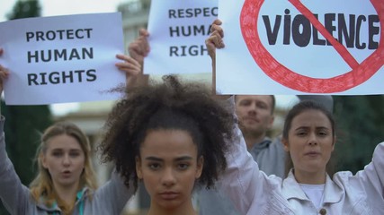 Afroamerican girl holding No racism sign, activists chanting Human rights slogan