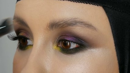 Fashionable multi-colored eye shadow chameleon with yellow purple gray silver color on the eyelid of a beautiful girl model with brown eyes. Professional cosmetic makeup. Eye close up view