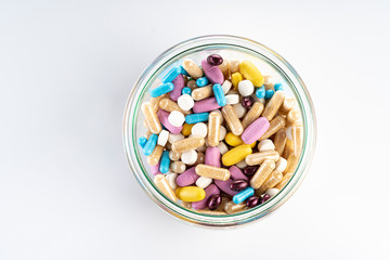 Glass jar full of medicines isolated on a white background. Blue, yellow, purple, white, brown tablets. Diseases