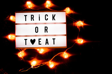 Trick or treat conceptual halloween photos, with a led board with the text trick or treat, with heart symbol instead of r,  and a wreath of illuminated small orange skulls on an orange background