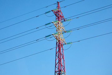 A red-white pole of a high voltage power line with wires and insulators opposite a bright blue sky. Energy and technology.