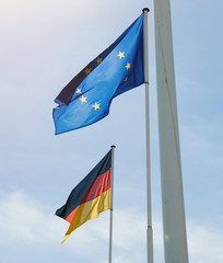 German and European Union flags waving with clear blue sky in the background at the border between France and Germany