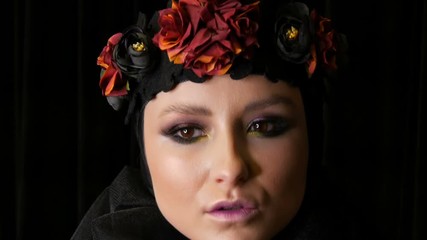 Professional girl model with beautiful makeup poses in a black cap and wreath on her head in front of the camera on a black background in the image of a black widow. High-fashion