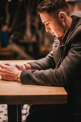 Fototapeta premium Young man in coat sitting by table at cafe