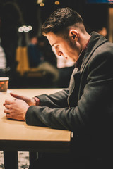 Young man in coat sitting by table at cafe