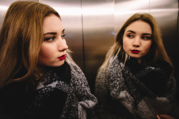 Young woman in warm clothing looking in the mirror in the elevator © finwal89
