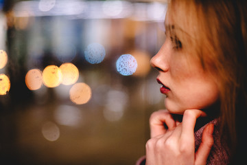 Young woman wearing warm clothing looking through window at night