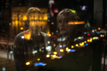 Reflection of two young women looking through window at night city
