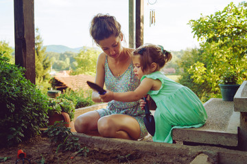 Young mother and daughter digging picking ground dirt land in their yard garden near the home house...