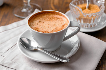 cup of coffee close-up with spoon,  saucer,  brown sugar  bowl and linen napkin on wooden table