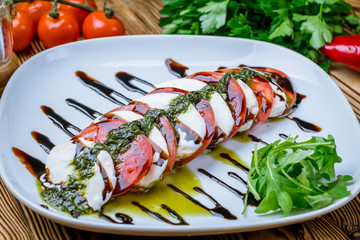 Caprese salad with mozzarella and tomato and sause pesto on wooden table