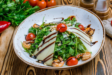 Arugula with shrimps and tomatoes on wooden table