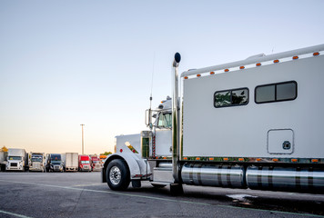 Big rig white powerful semi truck with comfort long sleeping compartment standing on truck stop for...