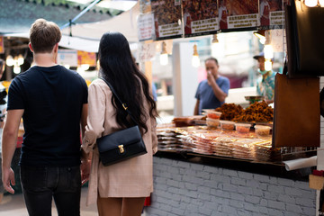 Asian woman and Caucasian Man from diverse culture shopping and eating street food outdoor during vacation and travel in Summer together, blur background selective focus