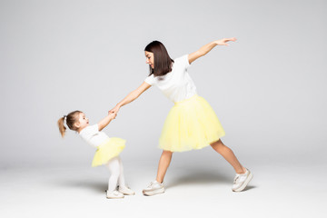 Full-length shot of cheerful adult lady and little girl in light dresses dancing on isolated white background