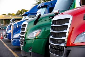 Different make big rig semi trucks tractors stands in row on truck stop parking lot marked with...