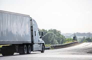 Big rig blue bonnet semi truck going with refrigerator semi trailer on the road with forest and meadows