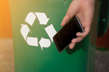 Man holding phone in hand next recycle bin 